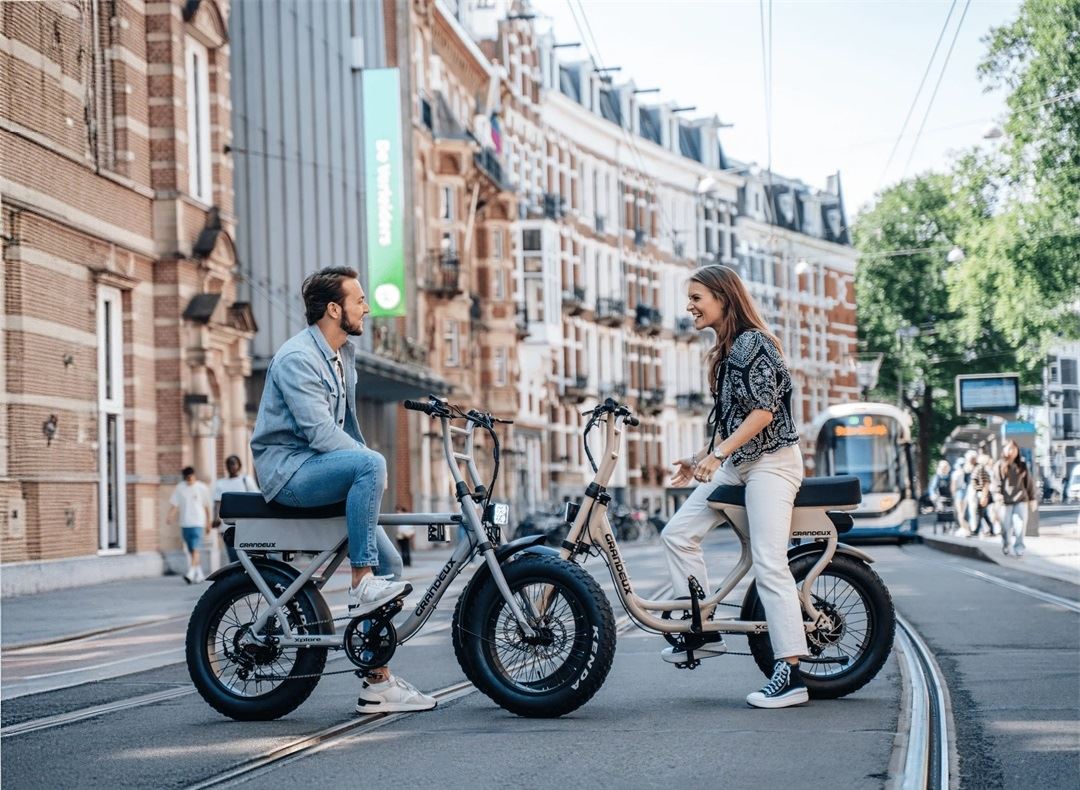 Man and woman riding Grandeux X-Series electric bikes, featuring the Xcite step-thru and Xplore over-frame models, designed for city commuting and urban adventures